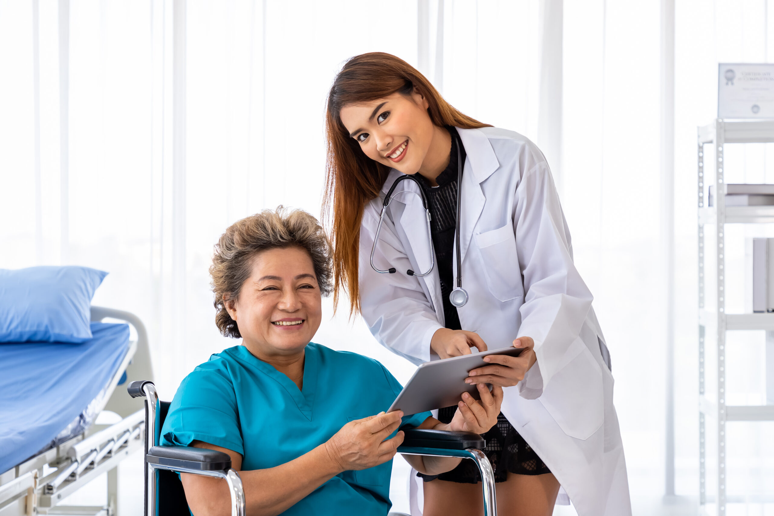 Asian medical doctor take care and explain senior elderly woman female patient on wheelchair with tablet, looking at camera